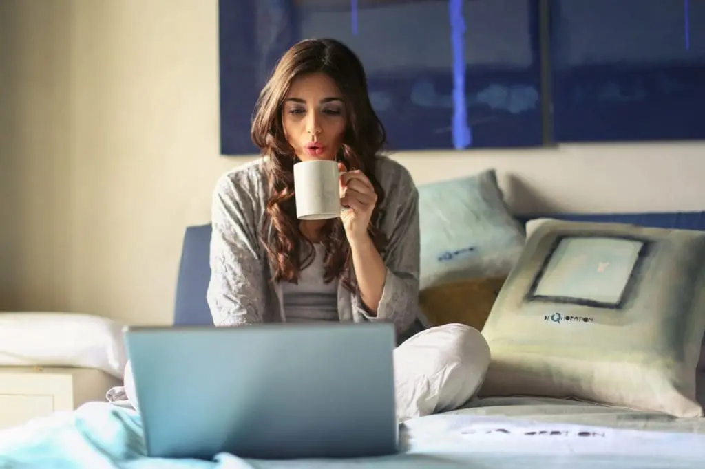 woman in grey jacket sits on bed uses grey laptop 935743