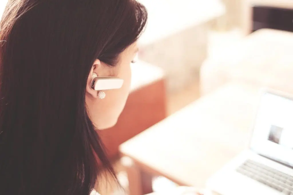 woman wearing earpiece using white laptop computer 210647