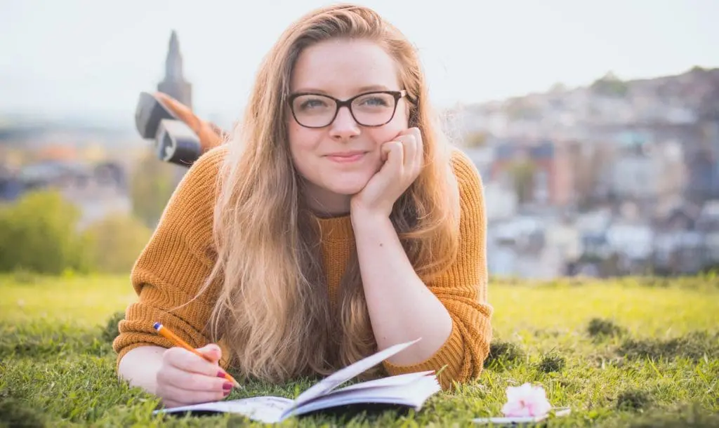 woman lying on green grass while holding pencil 1458318