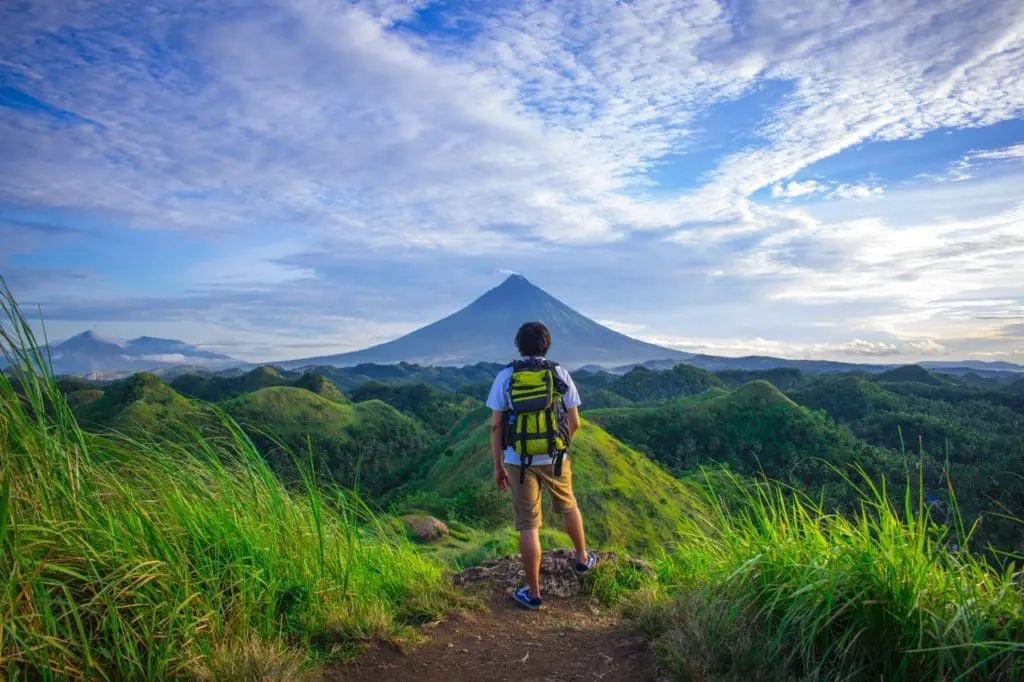 man wearing white shirt brown shorts and green backpack 672358